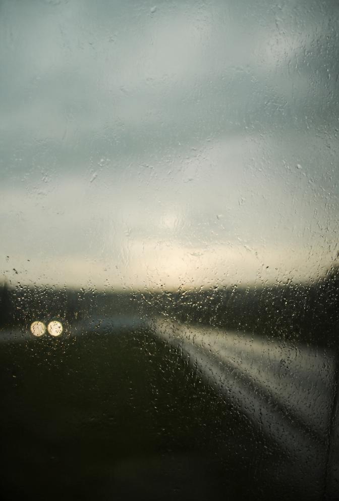 Rain-flecked window looking onto a dim landscape at dusk